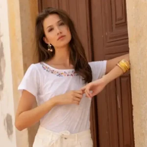 T-shirt blanc en coton avec broderies colorées autour de l’encolure, porté par une femme dans un style estival.
