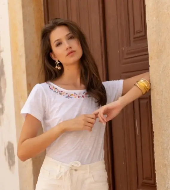 T-shirt blanc en coton avec broderies colorées autour de l’encolure, porté par une femme dans un style estival.