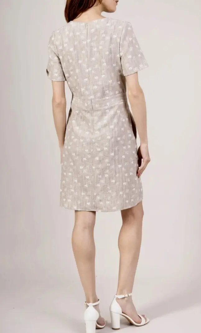 Vue de dos d’une femme portant une robe beige courte à manches courtes et motifs discrets.