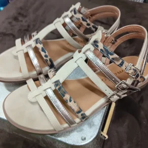 Sandales beiges à brides croisées avec finitions dorées et imprimé léopard posées sur un fond marron.