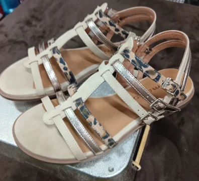 Sandales beiges à brides croisées avec finitions dorées et imprimé léopard posées sur un fond marron.